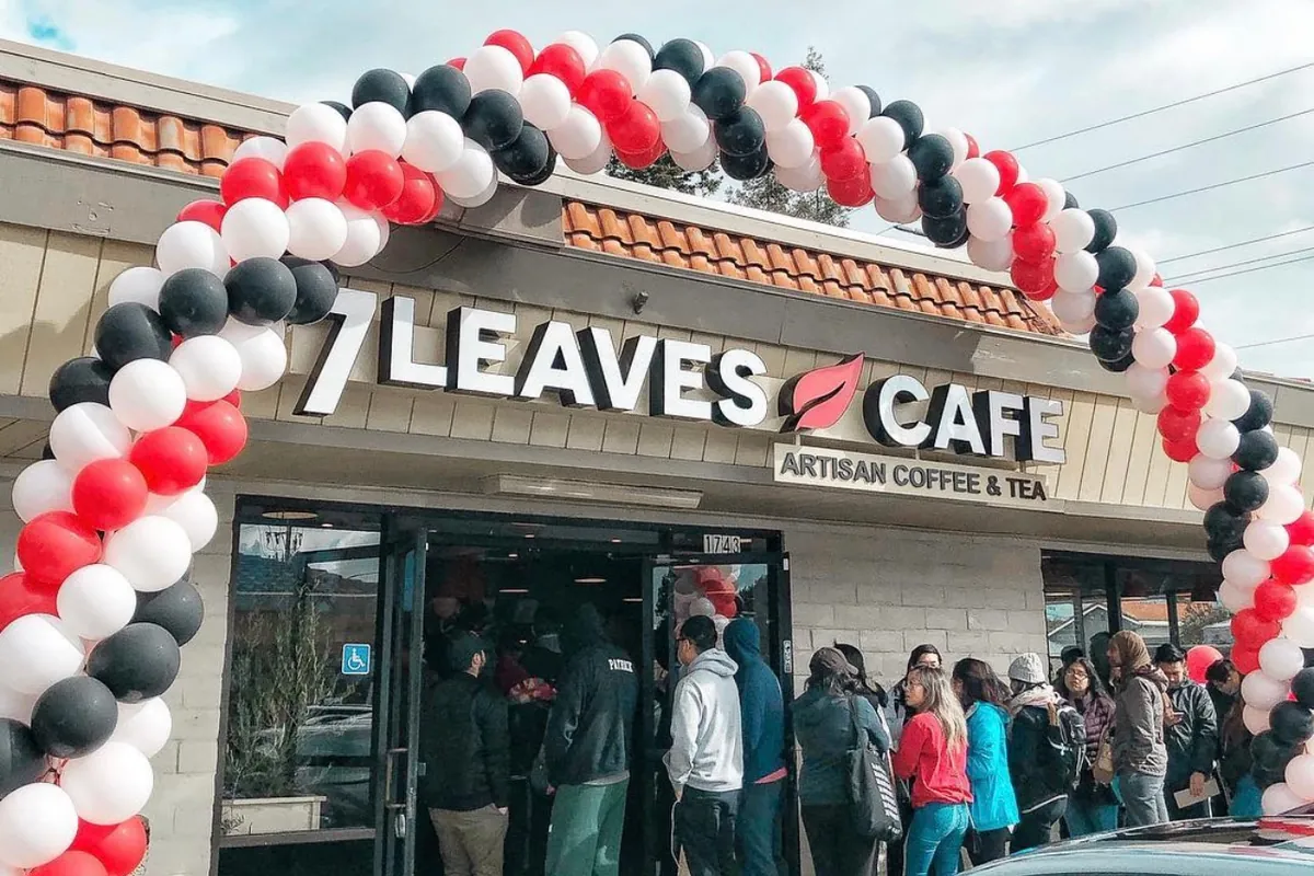 Customers lining up under a balloon arch at a 7 Leaves Cafe grand opening